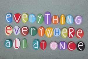Colorful stones with white letters spelling "everything everywhere all at once" on a sandy surface.